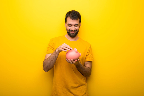 Man on isolated vibrant yellow color taking a piggy bank and happy because it is full - Photo, image