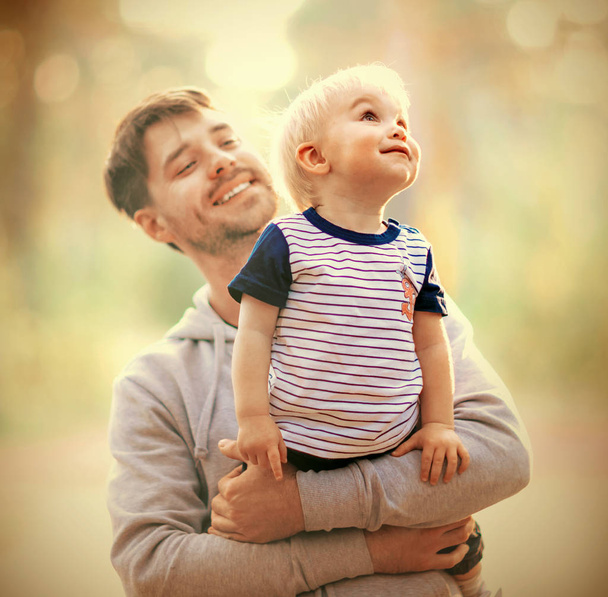 Young father holds his son. Man is having fun with his little baby in a summer park. - Foto, Imagen