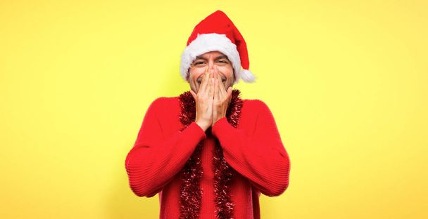 Человек в красной одежде празднует рождественские праздники улыбаясь много, прикрывая рот на желтом фоне
 - Фото, изображение