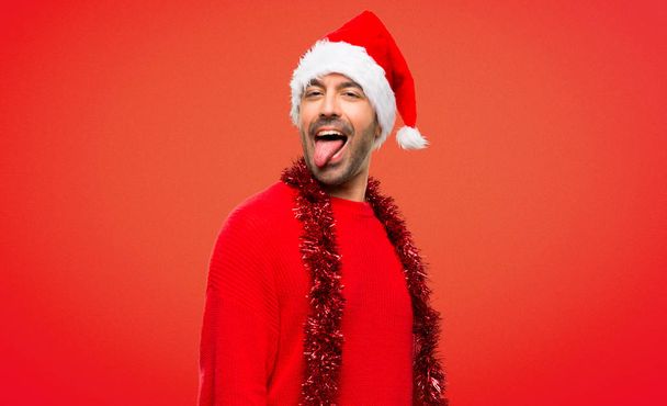 Людина з червоний одяг святкування різдвяних свят показує язик на камеру з забавний погляд на червоному тлі - Фото, зображення