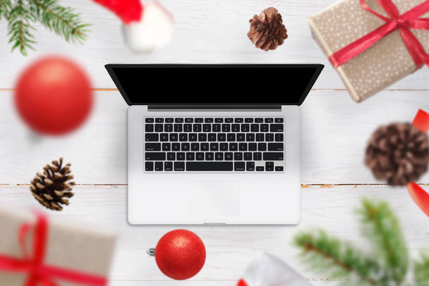 Christmas gifts and decorations come out of the laptop. An empty screen of the device for the mockup, web site design promotion. Top view of a wooden wooden desk. - Фото, изображение