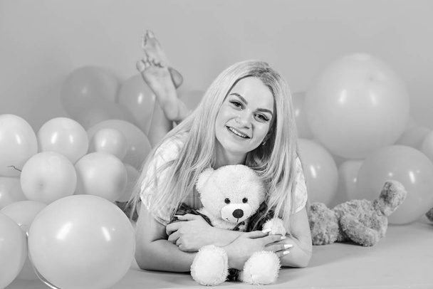 Girl in pajama, domestic clothes lay near air balloons, pink background. Blonde on smiling face relaxing with teddy bear toy. Birthday girl concept. Woman cute celebrate birthday with balloons - Фото, зображення