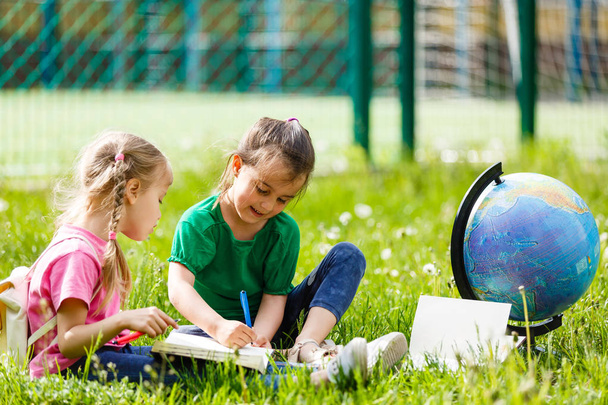 Два маленьких школярки, сидячи на траві з глобусом  - Фото, зображення