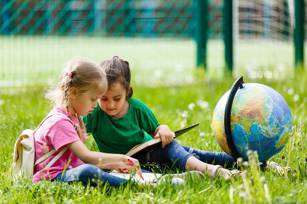 Due piccole studentesse sedute sull'erba con Globe
  - Foto, immagini