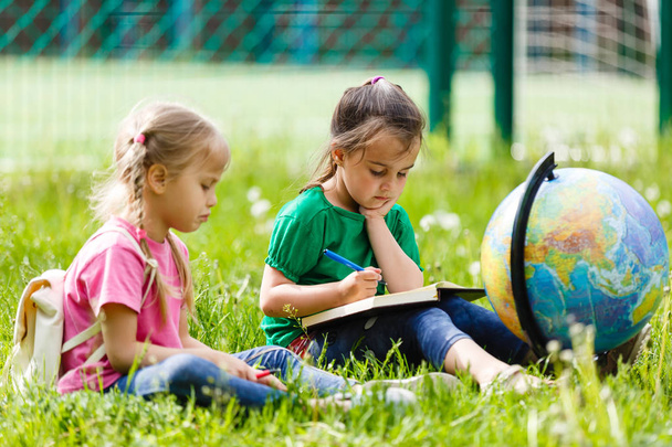 Two little schoolgirls sitting on grass with Globe  - Photo, Image