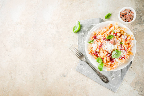Cuisine italienne, pâtes fusilli à la sauce tomate, fromage parmesan râpé et basilic, table en pierre claire
 - Photo, image