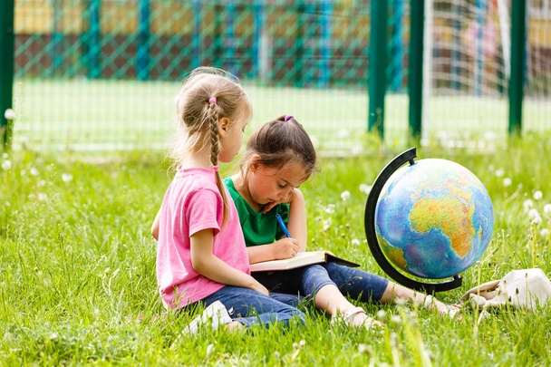 Twee kleine schoolmeisjes zittend op het gras met Globe  - Foto, afbeelding