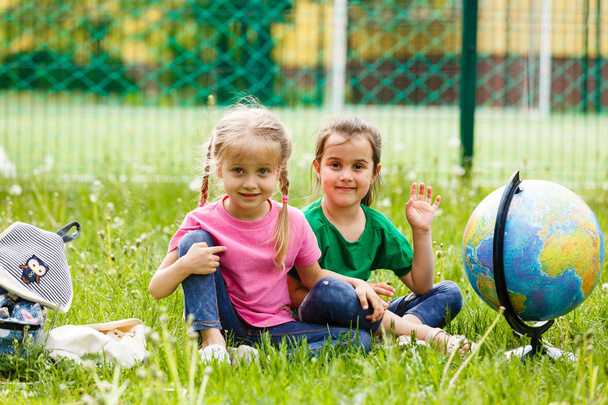 Two little schoolgirls sitting on grass with Globe  - Photo, Image