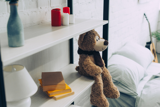 high angle view of teddy bear sitting on shelves with books and candles at home - Fotoğraf, Görsel