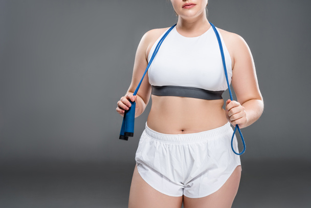 cropped shot of young oversize woman in sportswear holding jumping rope on grey - Foto, immagini