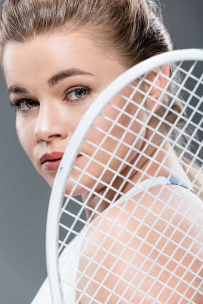 visão de perto da jovem segurando raquete de tênis e olhando para a câmera isolada no cinza
 - Foto, Imagem