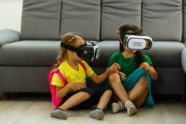 twee kleine meisjes met behulp van virtuele bril realiteit in huiskamer - Foto, afbeelding