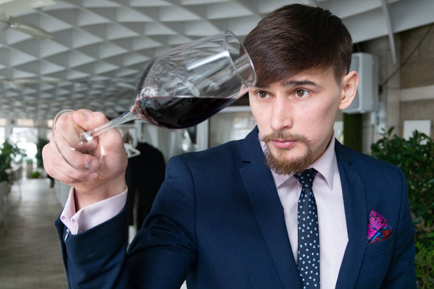 bir restoranda şarap tadımı bir kadeh kırmızı şarap genç erkek sommelier tutar - Fotoğraf, Görsel