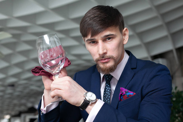 joven sommelier masculino sostiene una copa de vino tinto mientras degusta vino en un restaurante
 - Foto, imagen