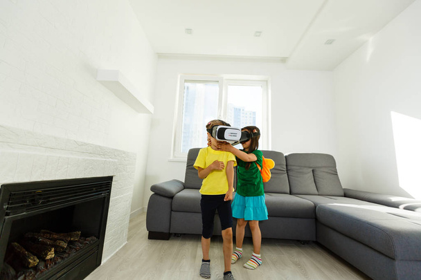 iki küçük kız sanal kullanarak gerçeklik evde oturma odasında gözlükler. - Fotoğraf, Görsel