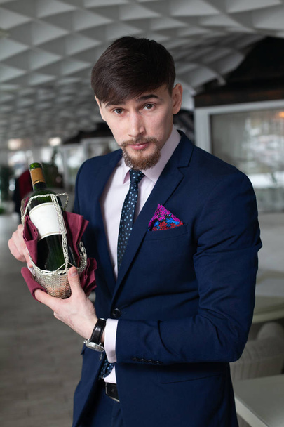 young male sommelier holds a bottle of red wine during wine tasting in restaurant - Photo, image