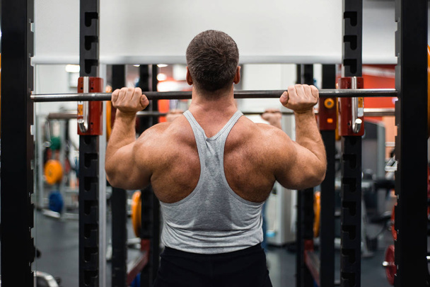 Big muscular man trains his shoulders with a barbell in the gym. Health and fitness concept - Foto, imagen