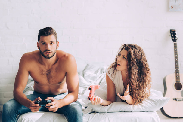 роздратована молода жінка жестикулює вручну, в той час як її концентрований хлопець грає у відеогру за джойстиком
  - Фото, зображення