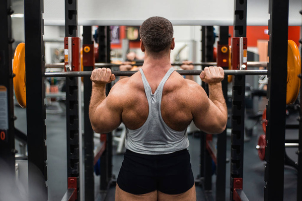 Big muscular man trains his shoulders with a barbell in the gym. Health and fitness concept - Foto, Imagem