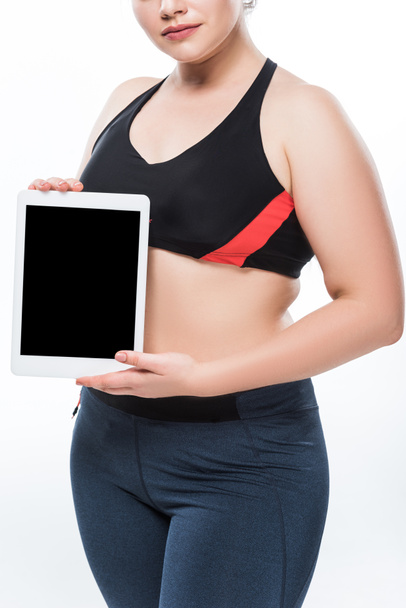 bijgesneden schot van overgewicht jongedame in sportkleding bedrijf digitale tablet met leeg scherm geïsoleerd op wit  - Foto, afbeelding