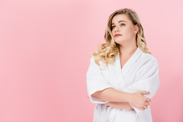 beautiful young oversize woman in bathrobe standing with crossed arms and looking away isolated on pink - Фото, изображение