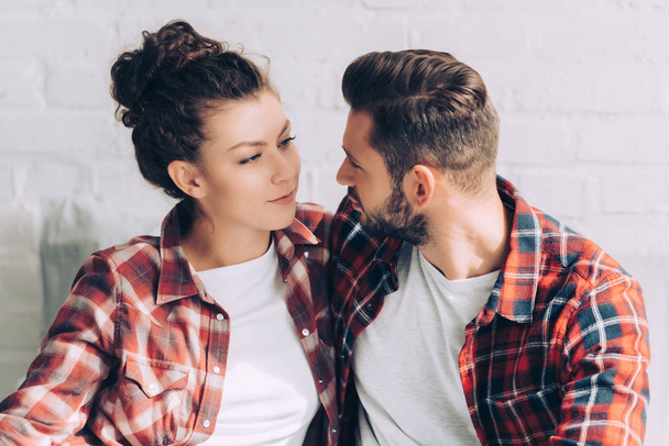 joyful young woman in checkered shirt embracing boyfriend at home - 写真・画像