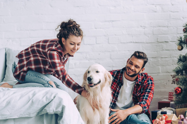 cheerful young couple petting cute dog on christmas at home  - Foto, Imagen