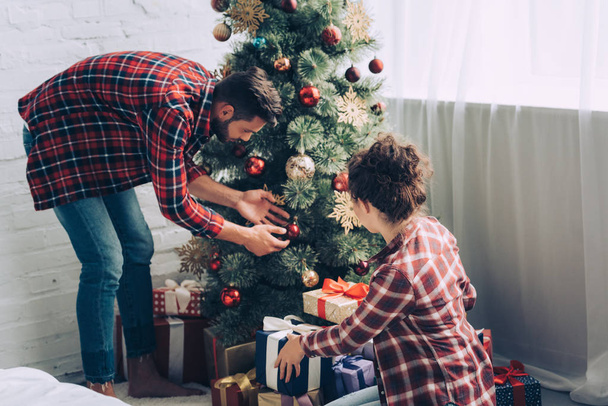 Paar in karierten Hemden schmückt Weihnachtsbaum zu Hause - Foto, Bild