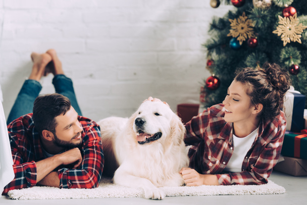 selective focus of cute golden retriever between happy young couple on christmas at home - Photo, Image