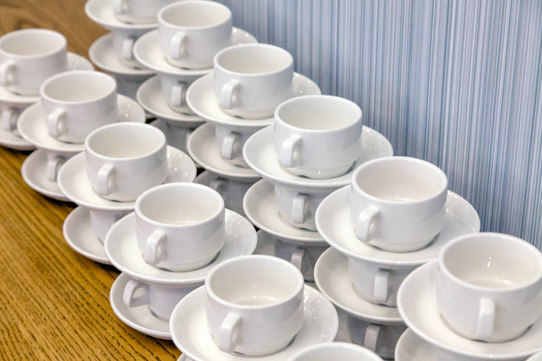 Un montón de pares de té de porcelana blanca en pilas en línea recta. Conferencia conceptual en el hotel, descanso, catering, desayuno
 - Foto, Imagen