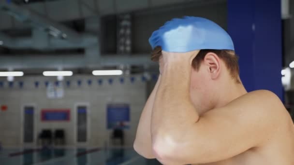 Side view a professional swimmer puts on a cap at an indoor pool - closeup slow motion shot - Footage, Video