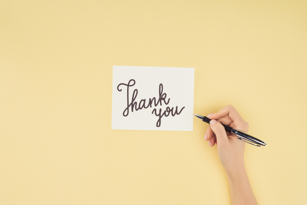 cropped person holding pen and white postcard with thank you lettering isolated on yellow background - Foto, immagini