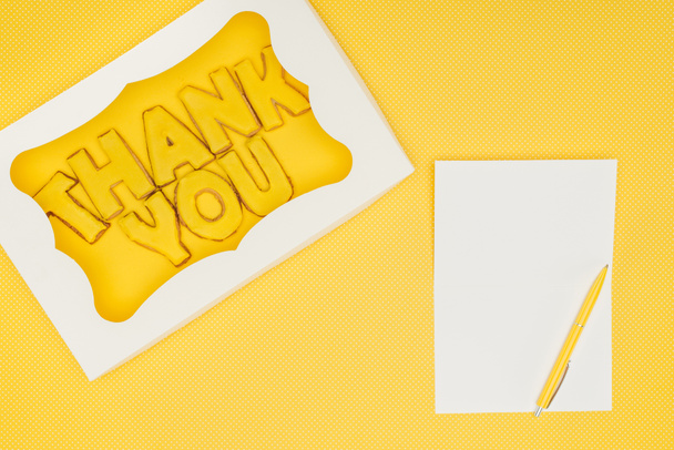 τετράγωνο σχήμα κέικ σε κουτί με γράμματα ευχαριστώ και σημειωματάριο που απομονώνονται σε κίτρινο φόντο - Φωτογραφία, εικόνα