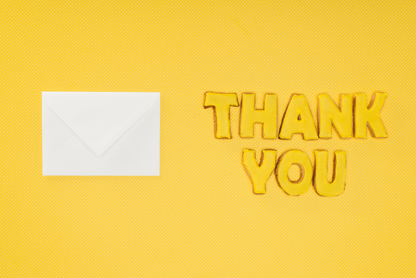 Ευχαριστώ γράμματα σε μπισκότα με κενό λευκό φάκελο που απομονώνονται σε κίτρινο φόντο - Φωτογραφία, εικόνα