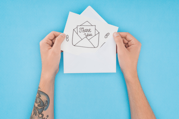 pessoa cortada segurando papel com obrigado lettering saindo do envelope isolado no fundo azul
 - Foto, Imagem