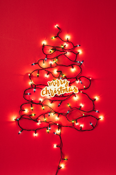 Guirlandes colorées en forme d'arbre de Noël avec signe de Joyeux Noël sur fond rouge
  - Photo, image