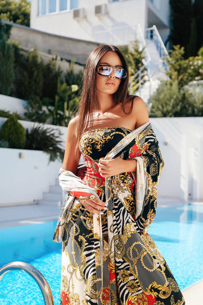 fashion outdoor photo of beautiful woman with dark hair in elegant swimming suit posing near swimming pool in white villa - Фото, зображення