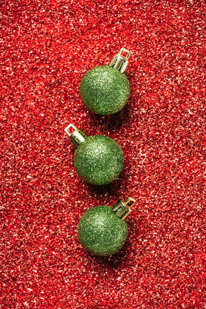top view of green shiny decorative christmas balls on red sequin background - Valokuva, kuva