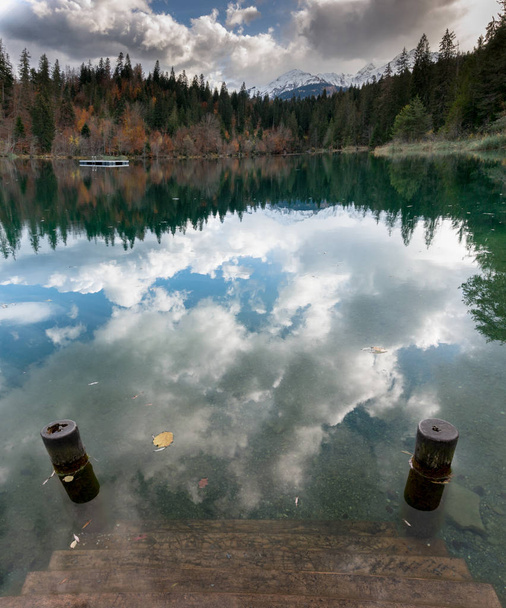 syksyllä väri metsä ja lehtien maisema ympäröivät idyllinen vuoristo järvi Alpeilla Sveitsissä myöhään syksyllä päivä heijastuksia vedessä ja puiset portaat johtavat veteen uimahalli
 - Valokuva, kuva