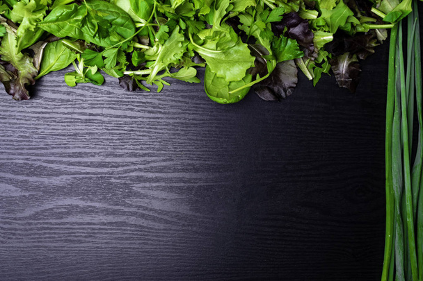 Auswahl an rohen Mikrogemüsen Spinat, Zwiebeln, Salat, Petersilie auf schwarzem Holzhintergrund, Kopierraum - Foto, Bild