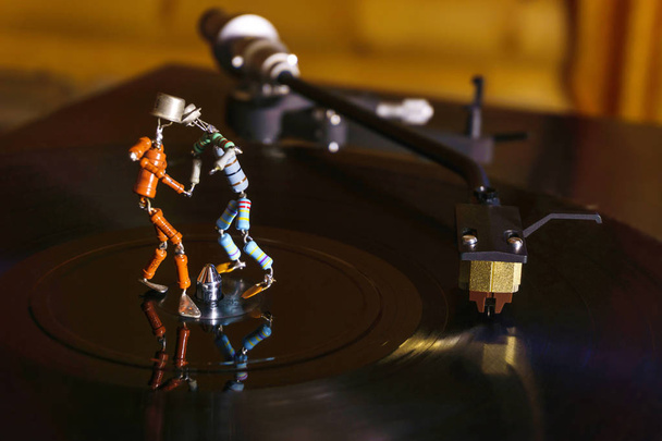 Zwei lustige kleine menschliche Figuren, grob aus Widerständen und Transistoren zusammengeschweißt, tanzen in der Dämmerung auf einer rotierenden Schallplatte; stilisiert als Vintage-Foto - Foto, Bild