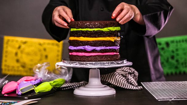 Step by step. Baker assembling a chocolate cake with bright colorful buttercream frosting for Dia de los Muertos holiday. - Photo, Image