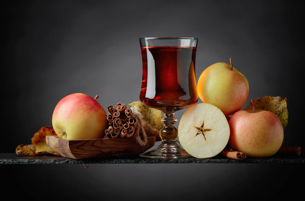 Glass of apple juice or cider with juicy apples and cinnamon sticks on a black background, copy space. - Photo, Image