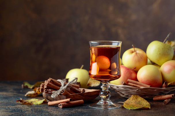 Ποτήρι χυμού μήλου ή μηλίτη με ζουμερά μήλα και ξυλάκια κανέλας σε ένα τραπέζι κουζίνας. - Φωτογραφία, εικόνα