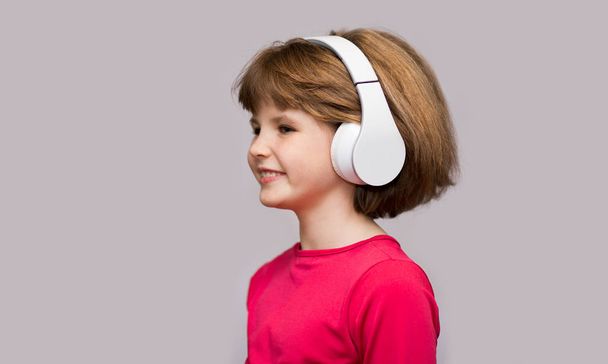 Happy smiling child enjoys listens to music in headphones over white background - Foto, Imagen