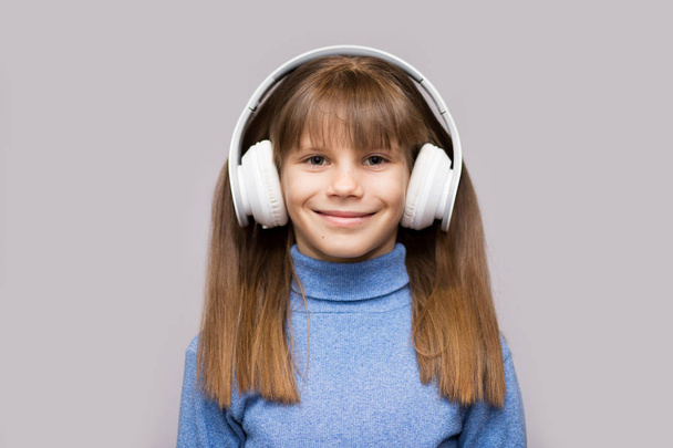 Criança sorridente feliz gosta de ouvir música em fones de ouvido sobre fundo branco
 - Foto, Imagem
