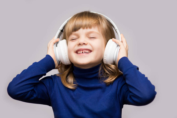 Energy kid girl with headphones listening to music with closed eyes on white background in studio.  - Photo, Image