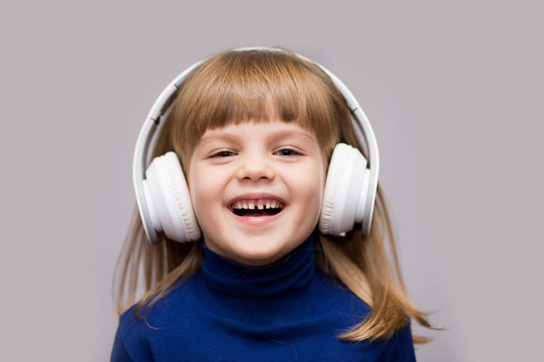 Šťastné usmívající se dítě těší poslouchá hudbu ve sluchátkách nad bílým pozadím - Fotografie, Obrázek