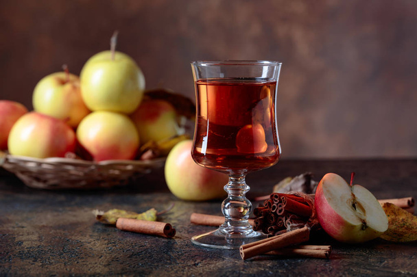 Glass of apple juice or cider with juicy apples and cinnamon sticks on a kitchen table. - Photo, Image