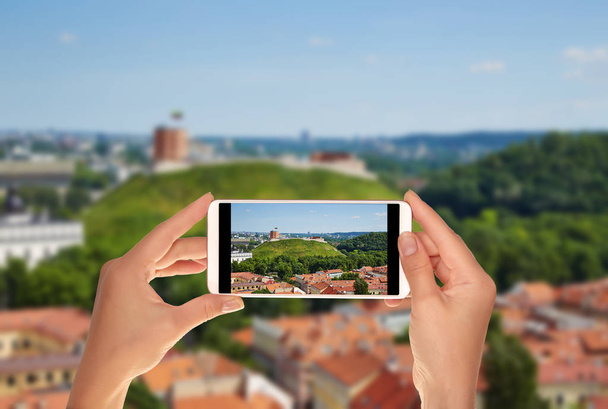 Un turista está tomando una foto del panorama de Vilna con una vista de la montaña del castillo en un día soleado de verano en un teléfono móvil
 - Foto, imagen